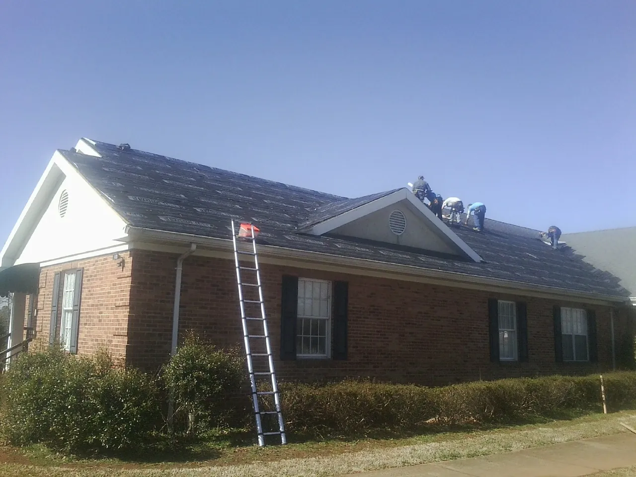 Crew tearing shingles off a brick ranch roof with a ladder set — Emergency Roof Repair work by our crew in Zumbrota