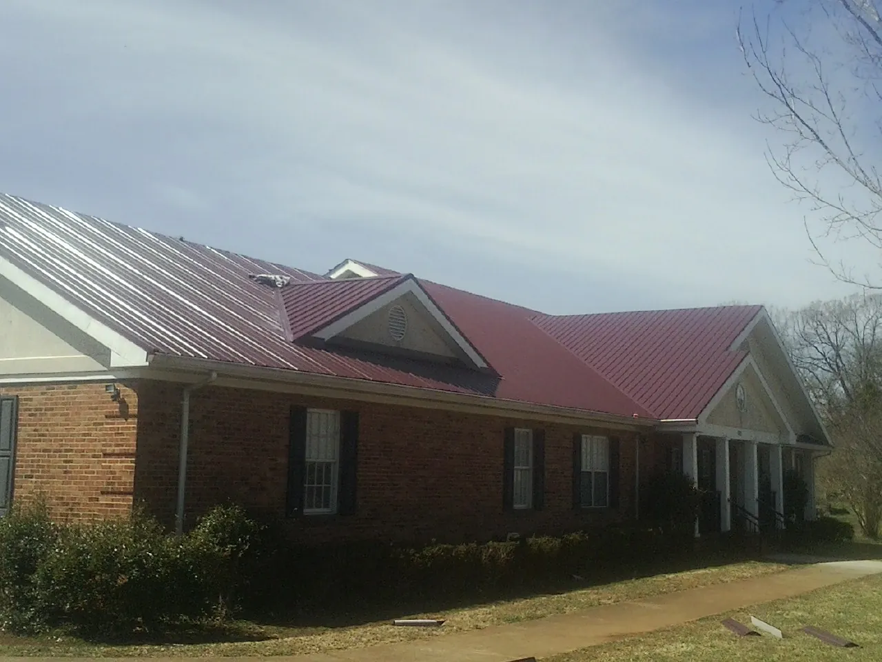 Red metal roof with gabled entries on a long brick building, from a Hail Damage Roof Repair job in Zumbrota