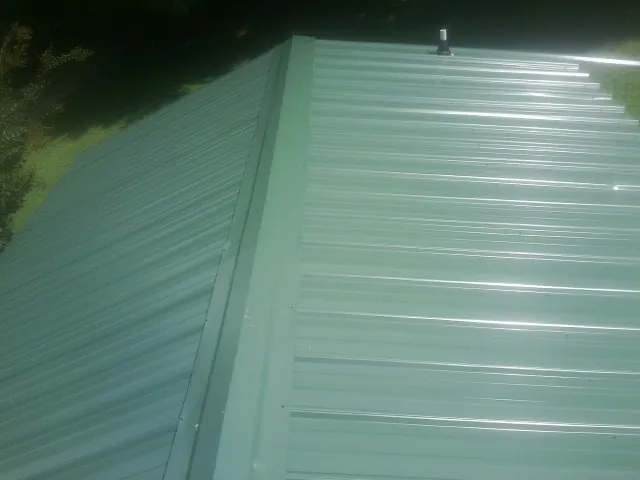 New green metal panels meeting at the ridge of a roof — Flat Roof Repair work by our crew in Zumbrota