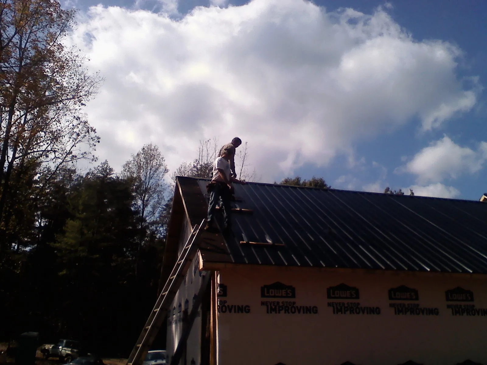 Roofer fastening dark metal panels high against a cloudy sky, from a Roof Inspection job in Zumbrota