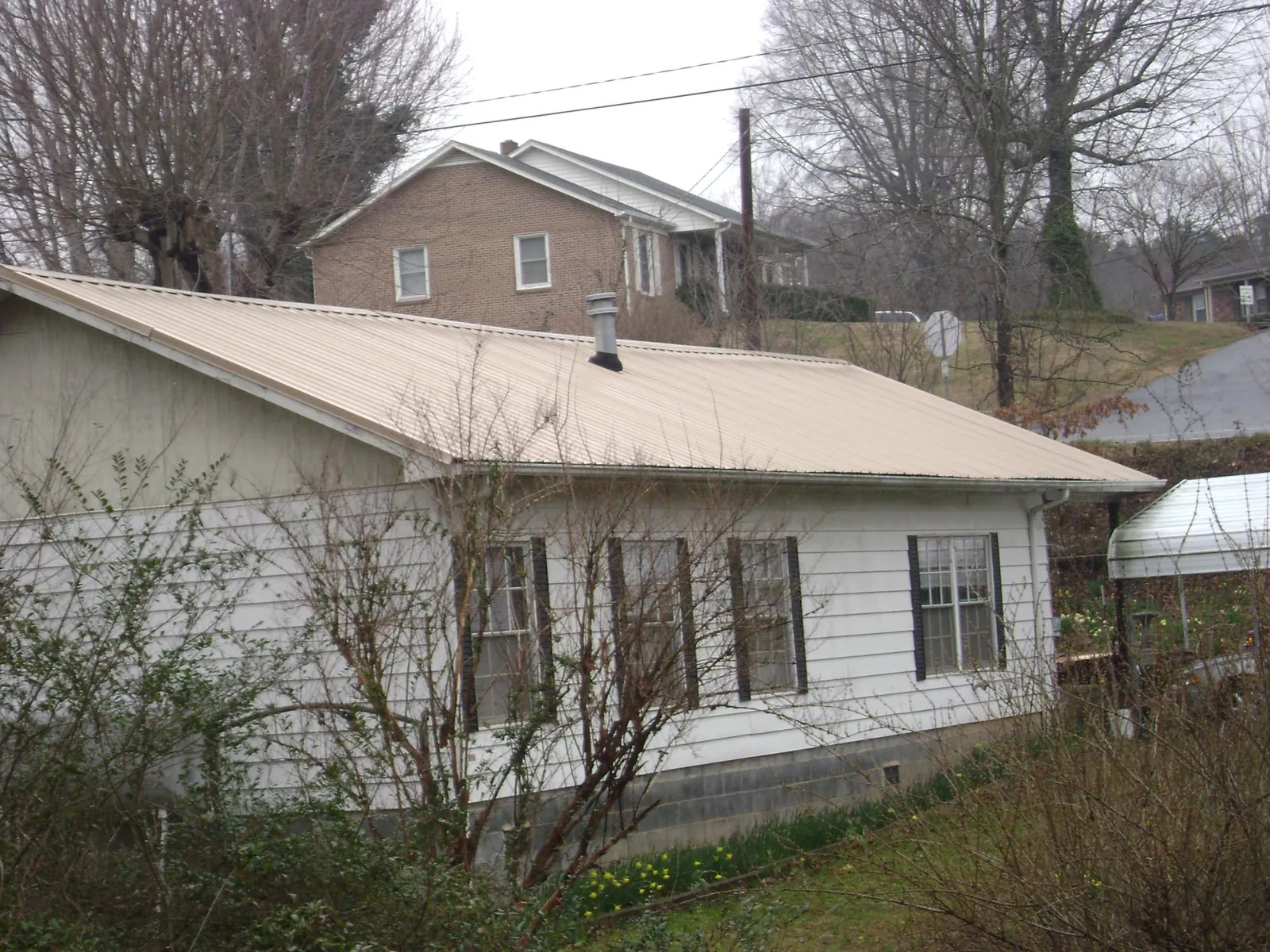 Tan metal roof on a white sided house set into a hillside — Commercial Roofing by Roofing Brothers in Zumbrota
